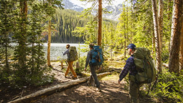 Three hikers walking through scenic woods wearing Kelty backpacking backpacks