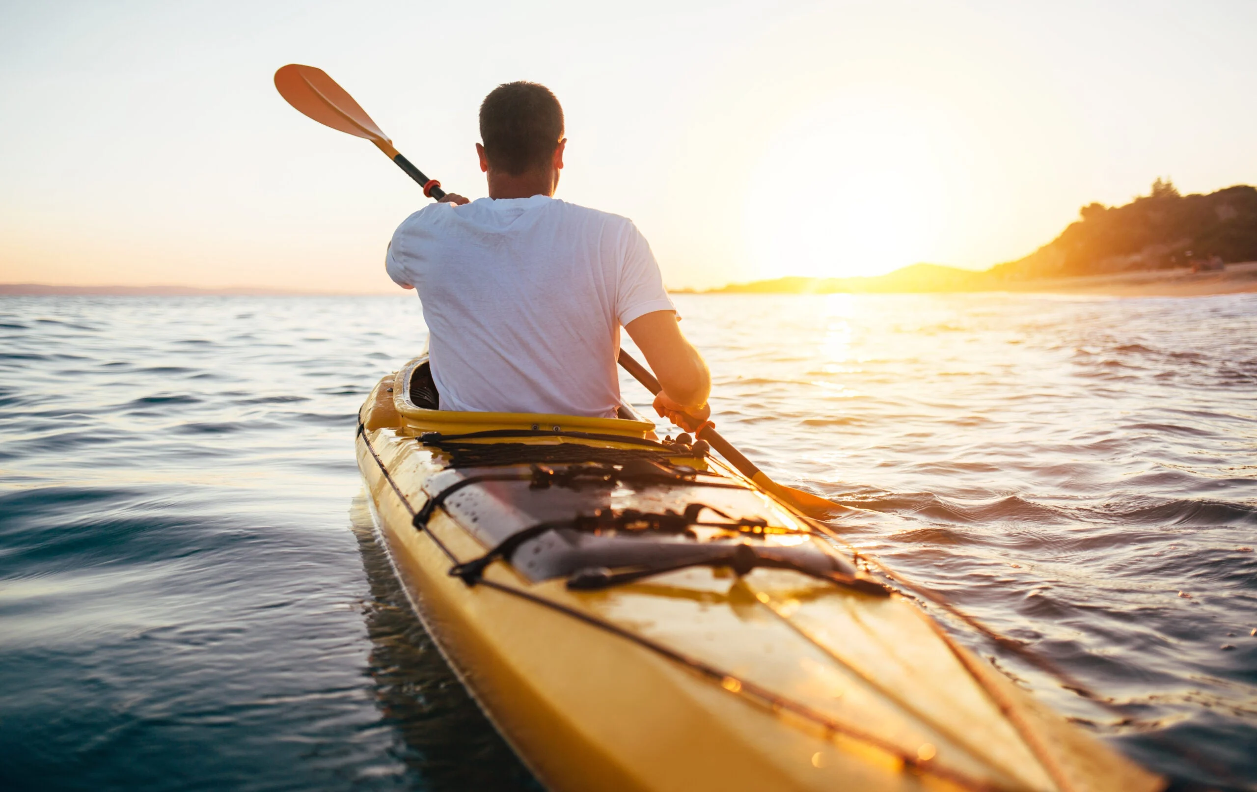 Man paddling a yellow kayak across a lake