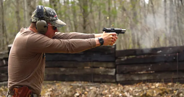 Man shooting a handgun in the woods.