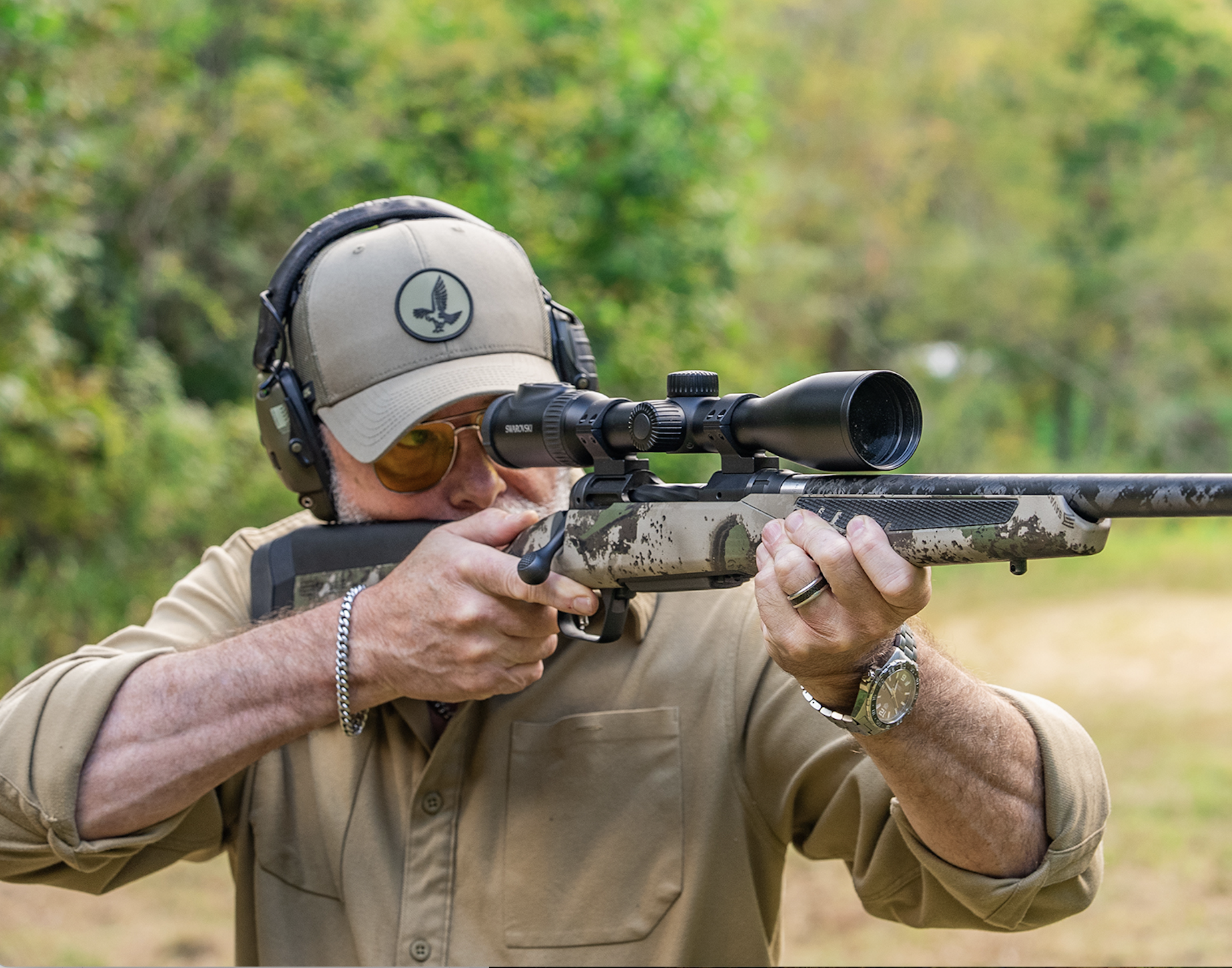 A shooter fires a bolt-action rifle in a field. 