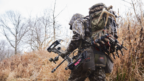 Hunter wearing Mystery Ranch backpack in the marsh carrying compound bow