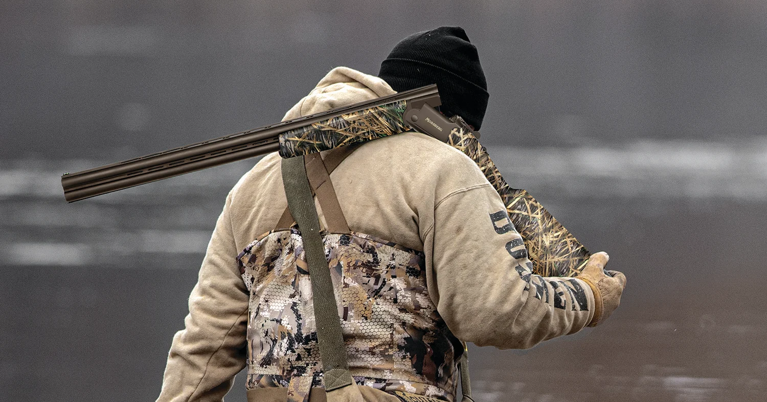 Waterfowl hunter walks with a Mossberg Silver Reserve Eventide shotgun over his shoulder.