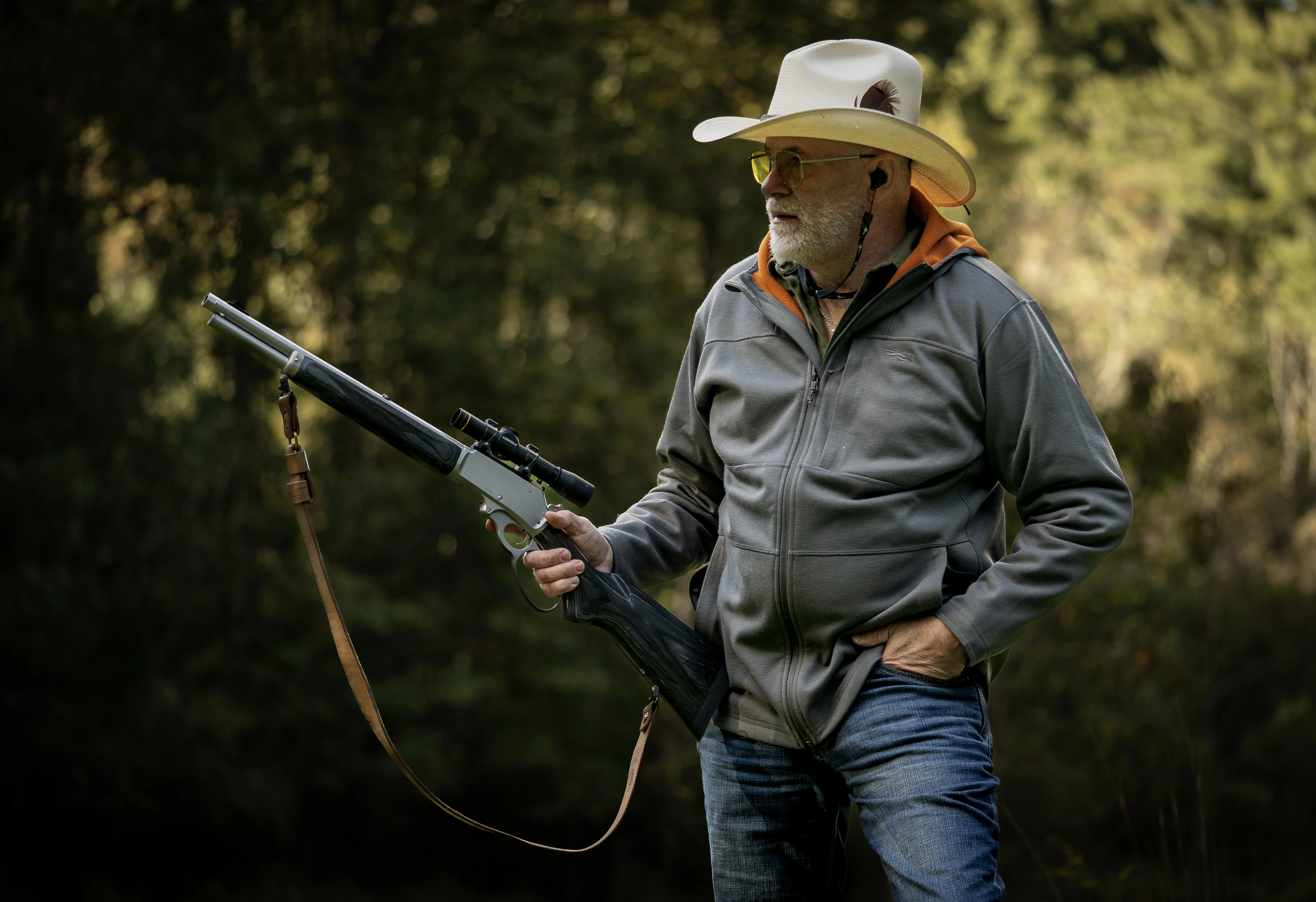 A shooter with a cowboy hat hold a lever-action rifle with a carry strap hanging from it. 