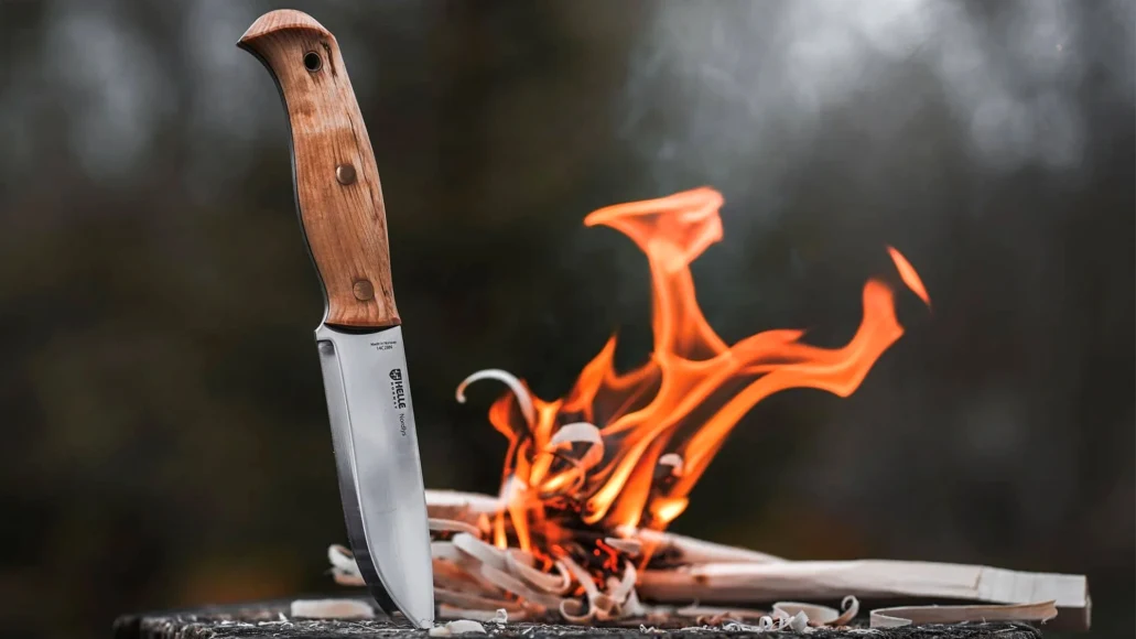 The new Helle Nordlys full-tang knife stuck into a log with fire in background. 