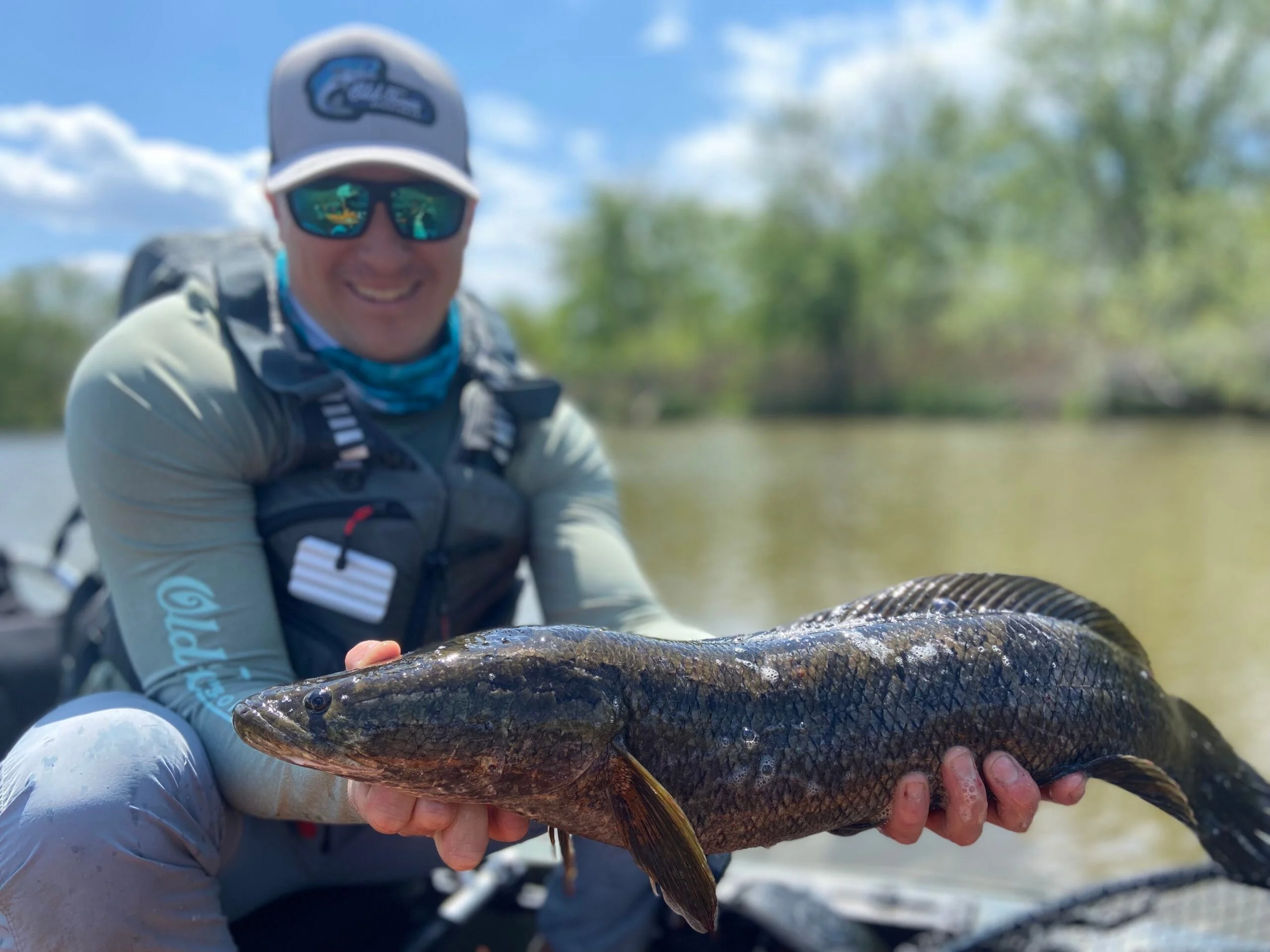 A fisherman wearing polarized sunglasses while holding a snakehead.