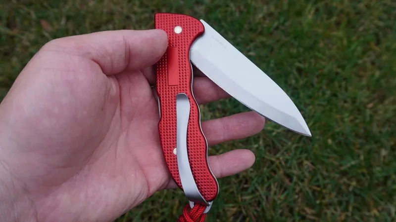 The red and silver Swiss Army Alox knife being held in a hand above a grass background. 