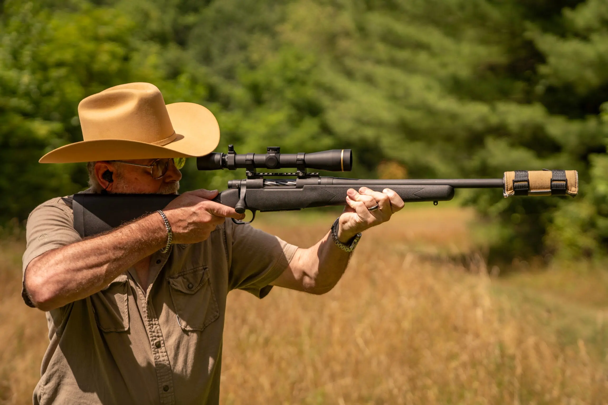 The author shoots a supressed Mossberg rifle with a field in background.