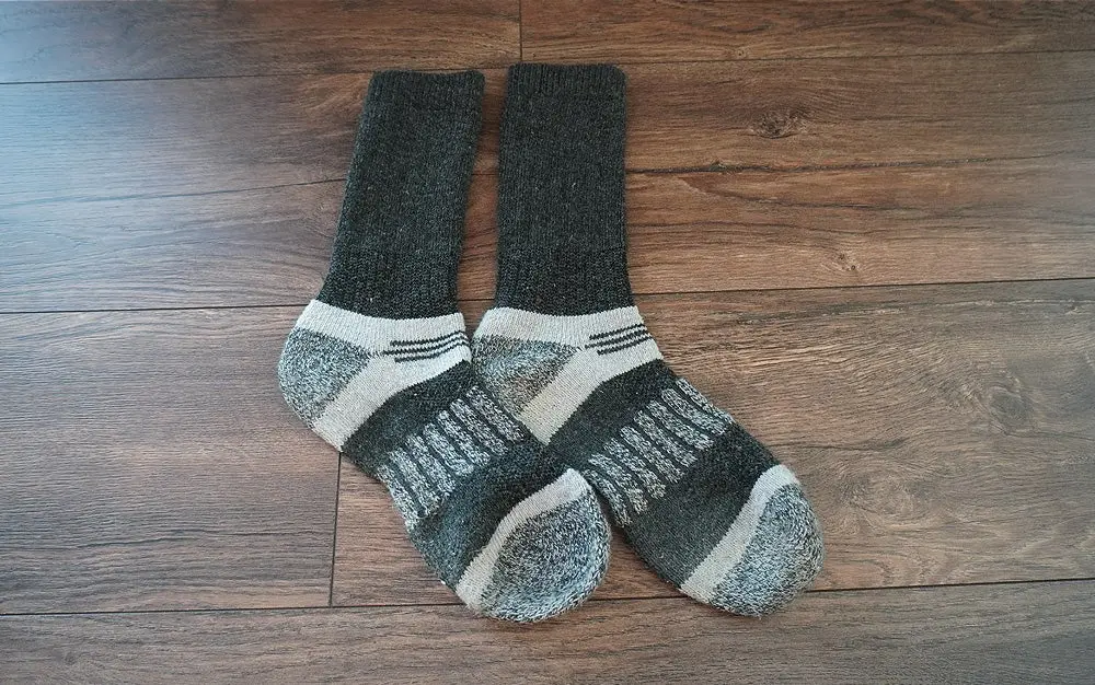 A pair of Magellan Outdoors Repreve hunting socks sitting on a dark wooden floor.