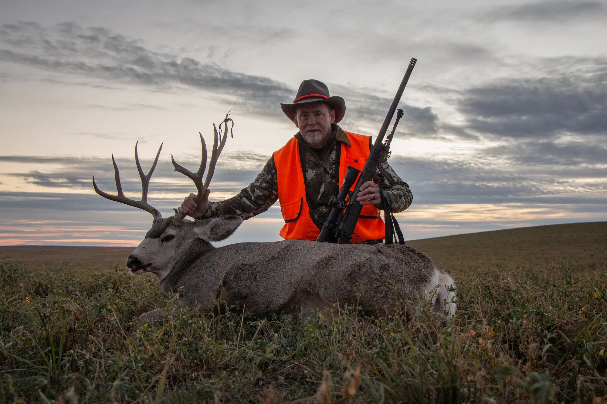 Man with a rifle next to a dead deer.