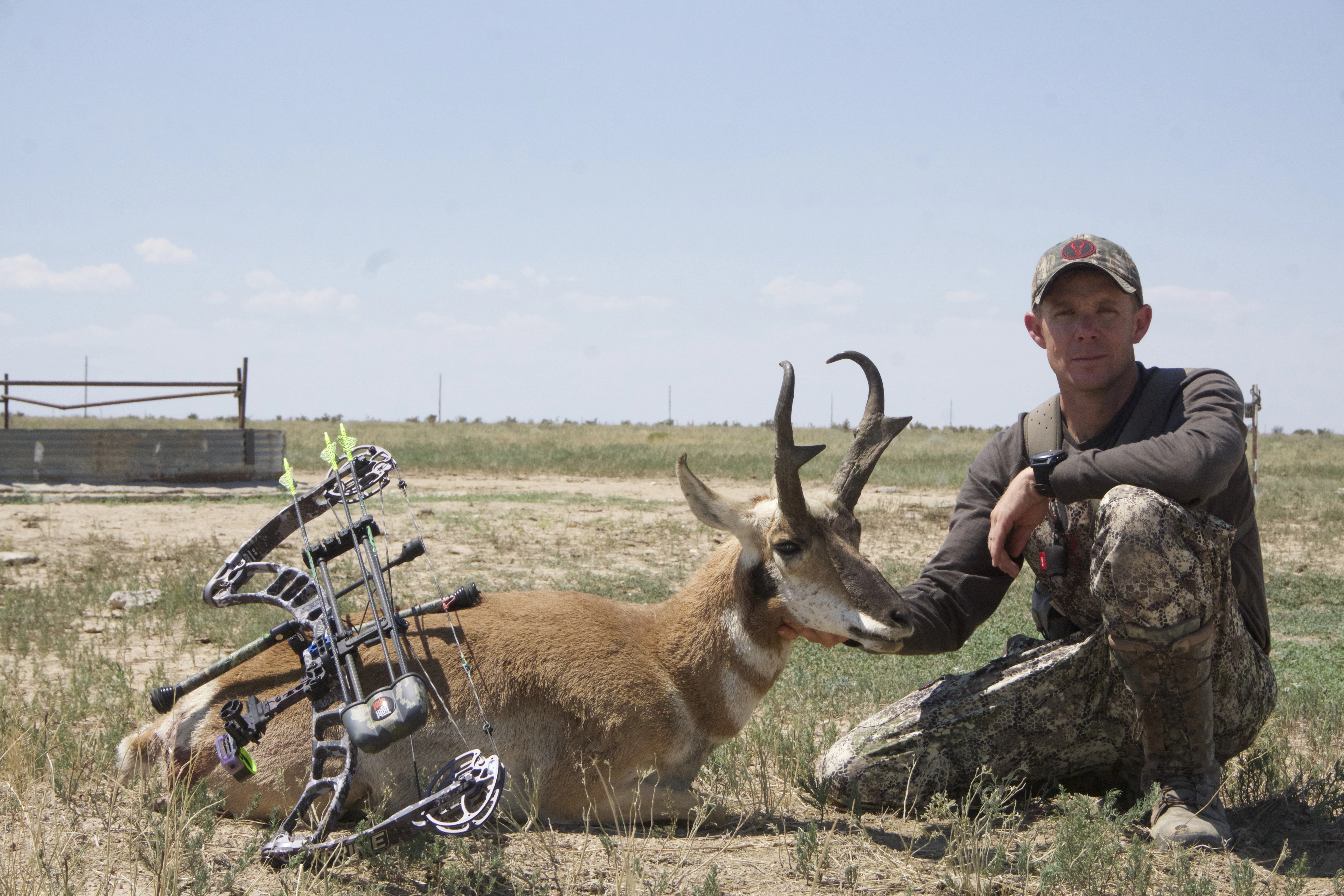 Bowhunter holds up a pronghorn buck with a water tank in the distance