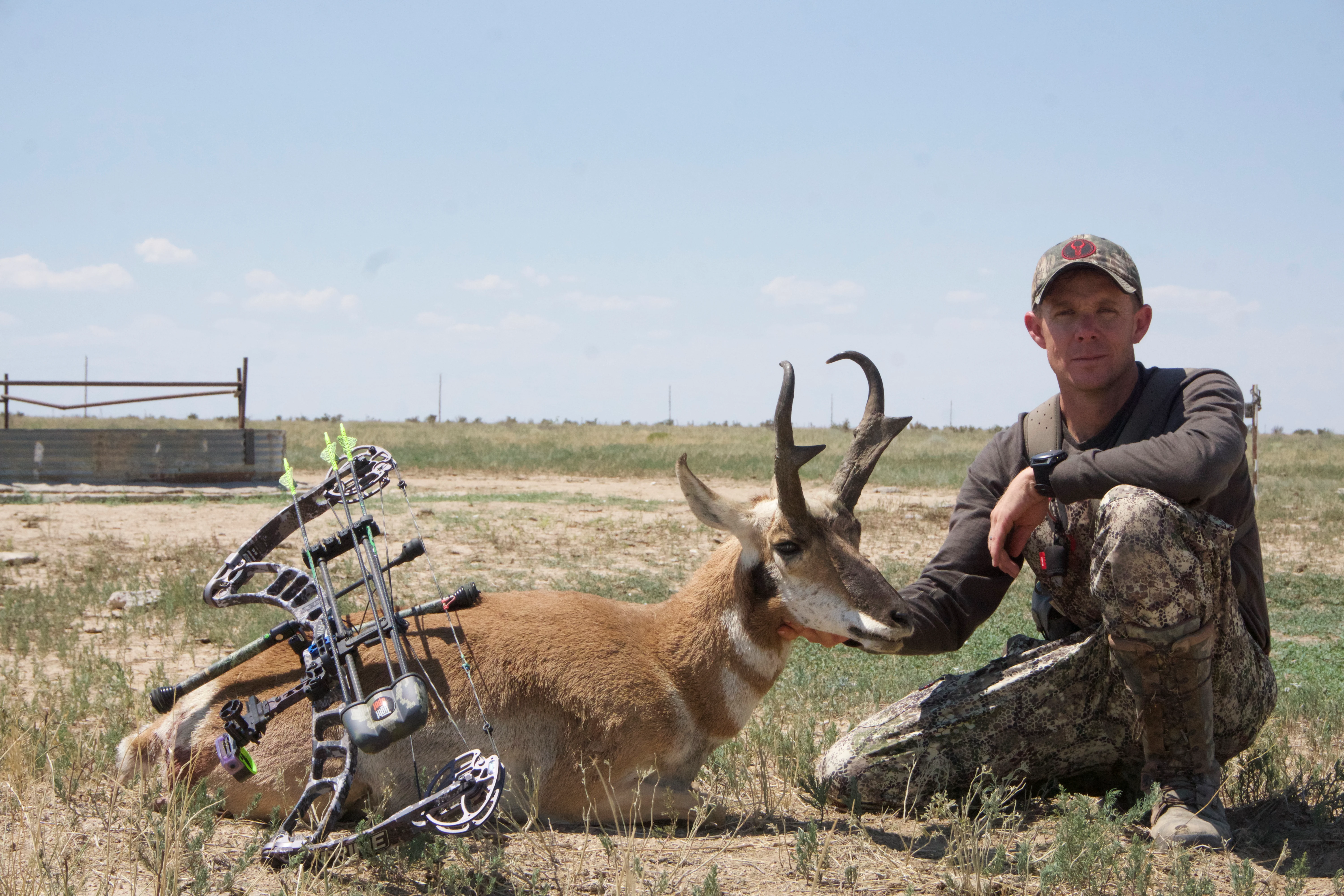 Bowhunter holds up a pronghorn buck with a water tank in the distance