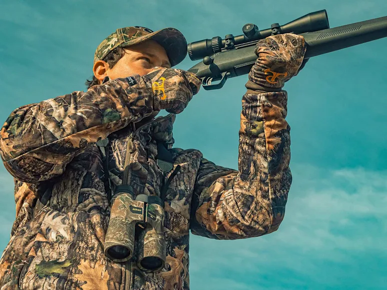 A hunter holds a rifle up to their shoulder.