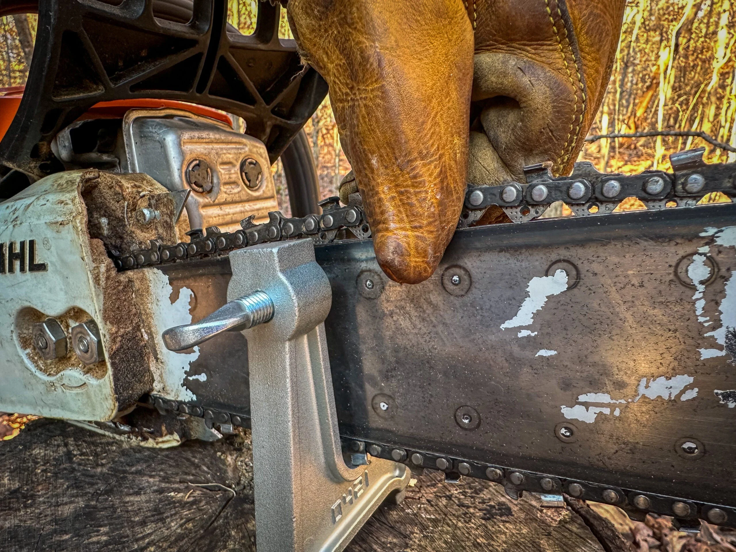 A gloved hand lifts the chain on a chainsaw