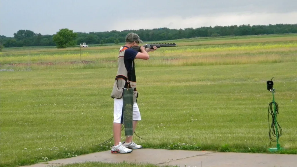 Boy holding shotgun standing on a shooting range.