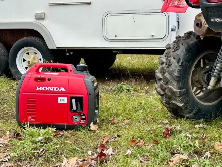 A Honda generator next to a camper and ATV at a camp site