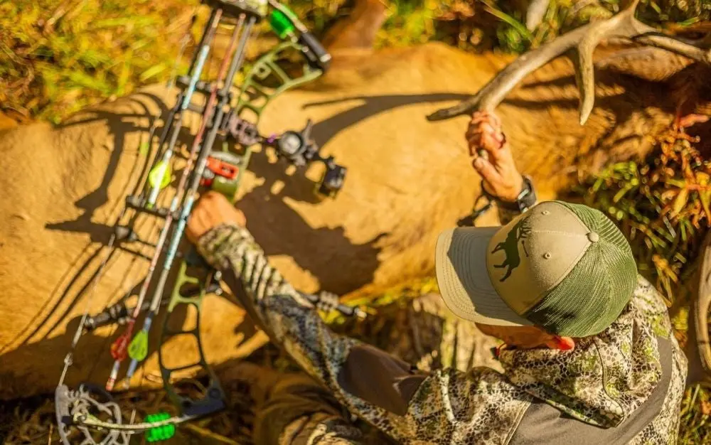 hunting holding elk in one hand and bow in another