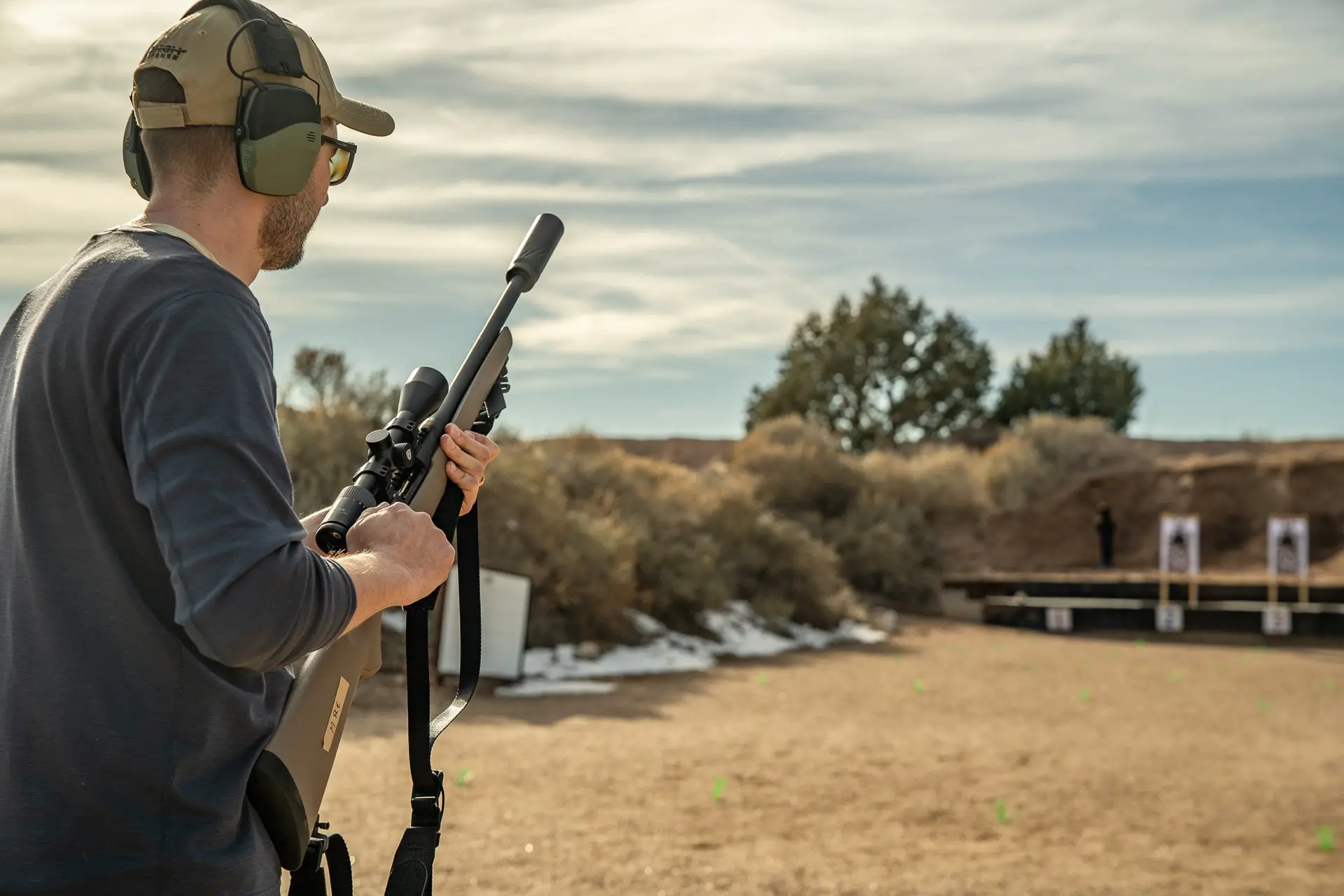 A shooter with a suppressed bolt-action rifle shoots offhand at a range