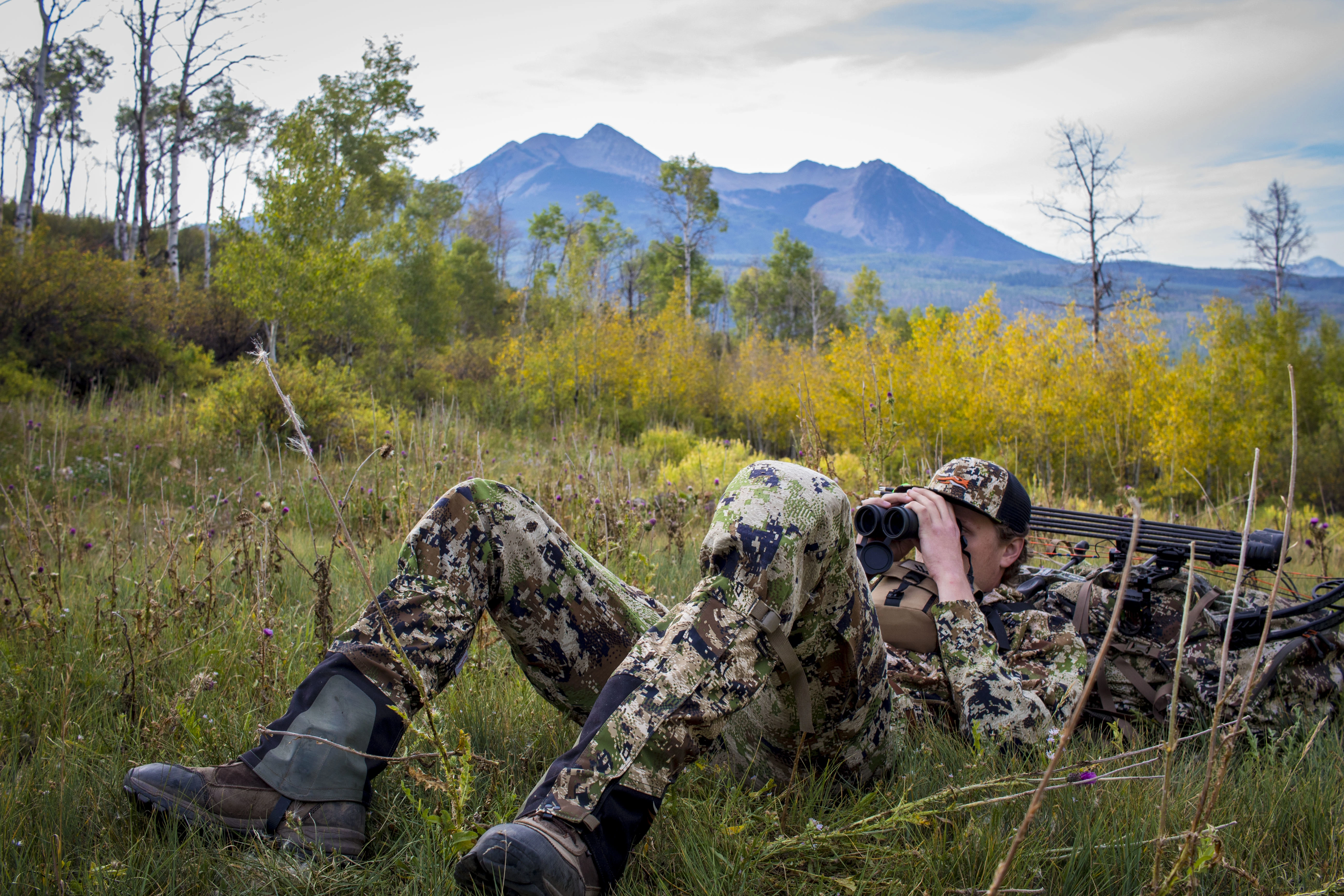 Hunting leaning on pack while looking through binoculars 