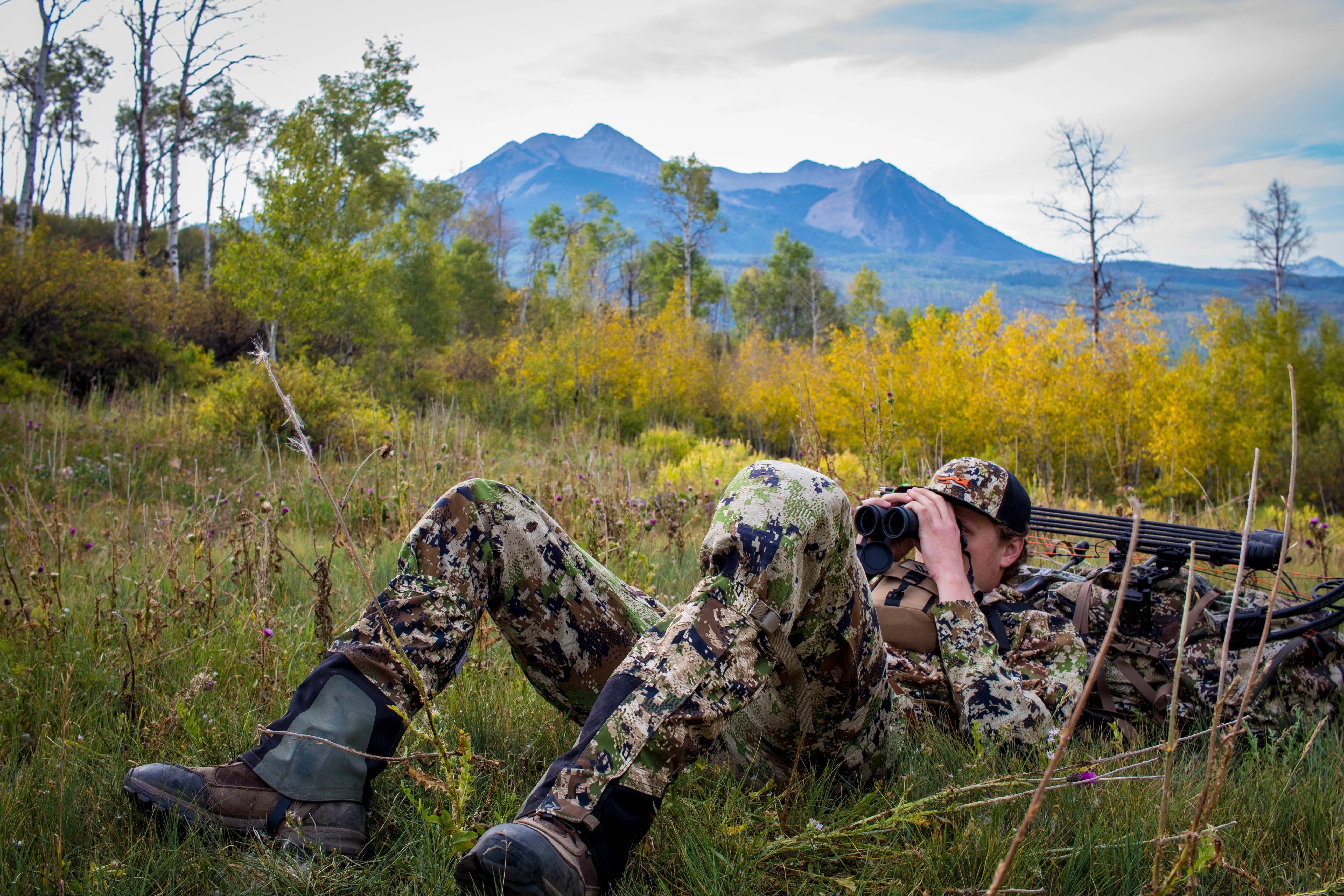 Hunting leaning on pack while looking through binoculars 