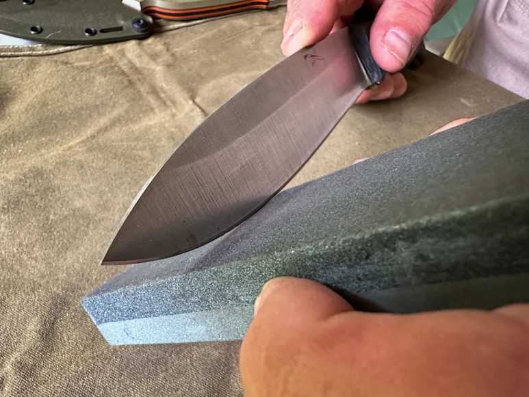 A man uses a stone to sharpen a knife