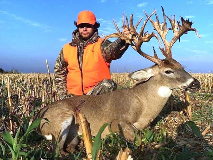 A hunter in orange and camo kneeling next to a large non-typical whitetail buck.