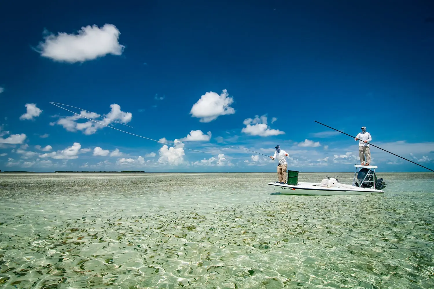 fully covered angler casts from the front of a flats boat as the guide holds a pole and stands on a platform behind him