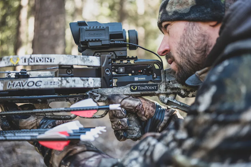 A hunter aims a crossbow in the woods.