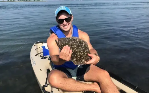 A man smiling and holding in his hands a big fish just sitting over a white kayak into the sea.