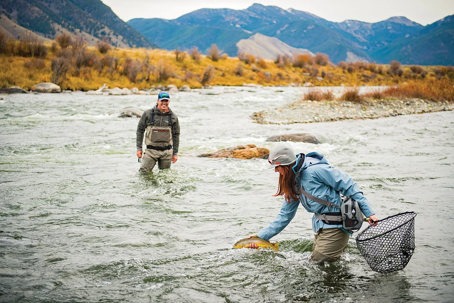 wading angler holding net prepares to release trout from hand; second angler looks on