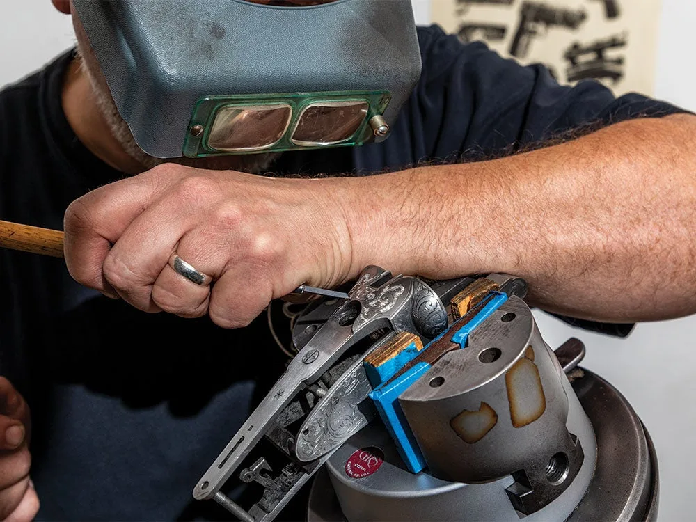 a gunsmith using a hammer and chisel to carve intricate patterns in a rifle barrel