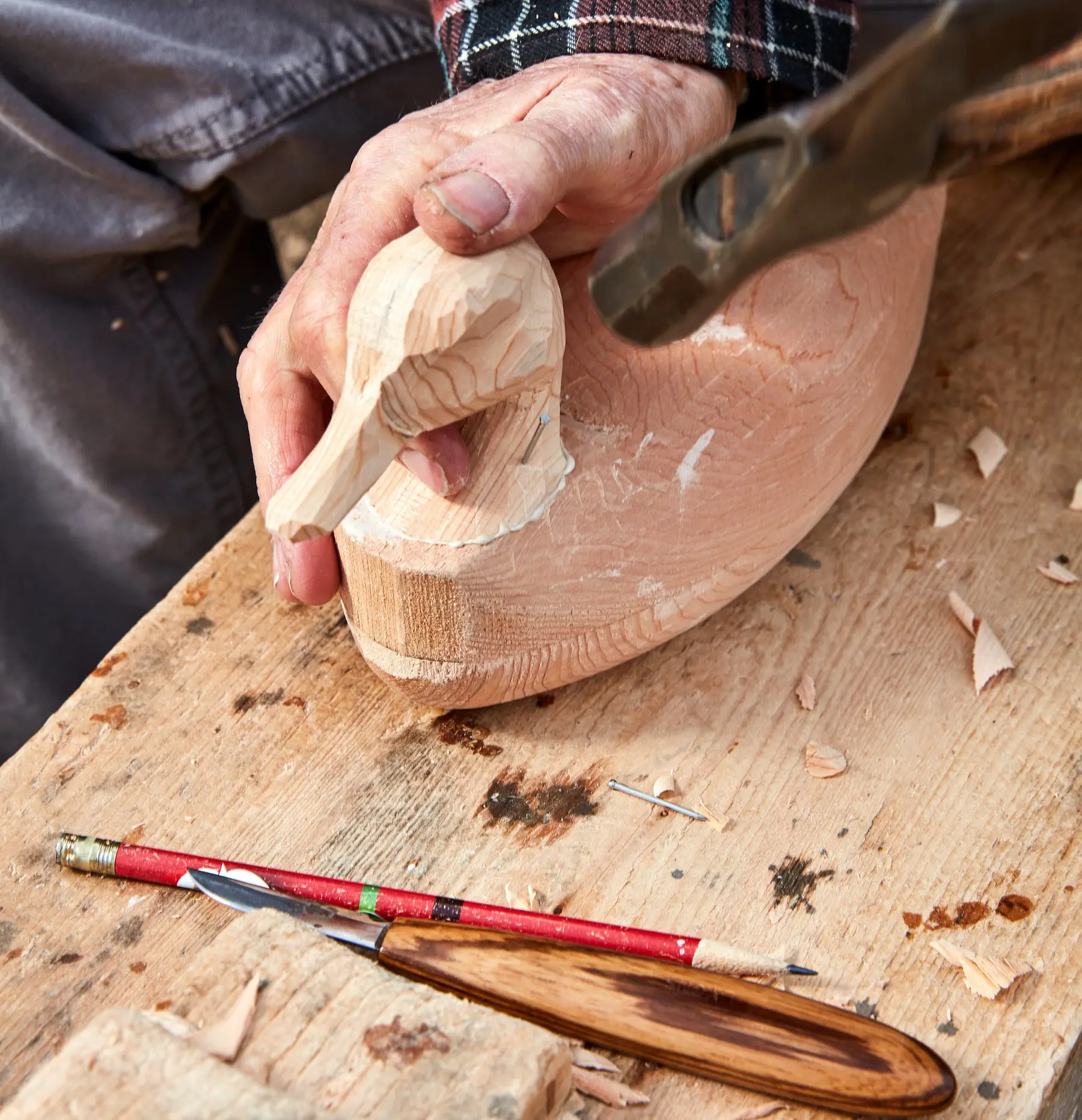 Hammering a duck decoy head onto a wooden body.