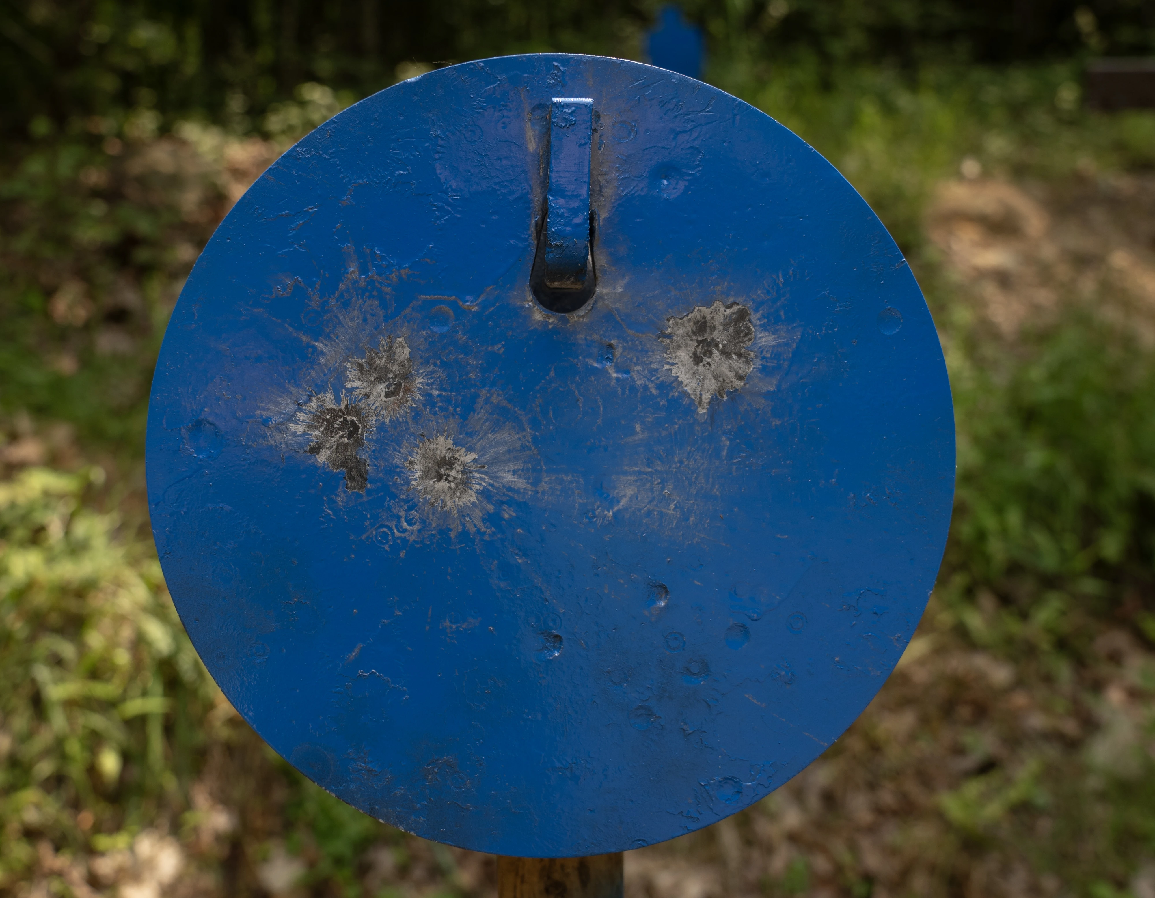 A blue steel plate target with gray bullet impacts on it. 