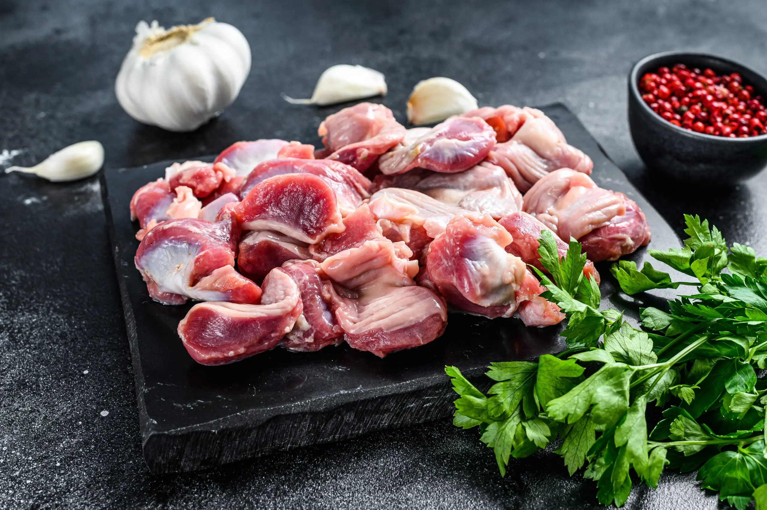 Raw chicken gizzards on a black, stone plate with herbs and spices