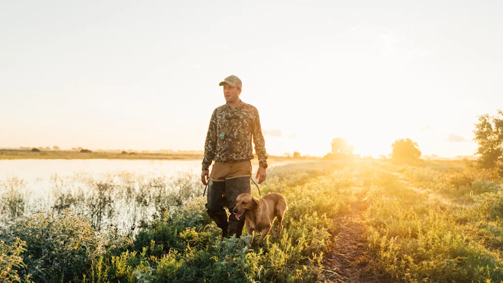 Sim Whatley, founder of Duck Camp, walking through field with dog