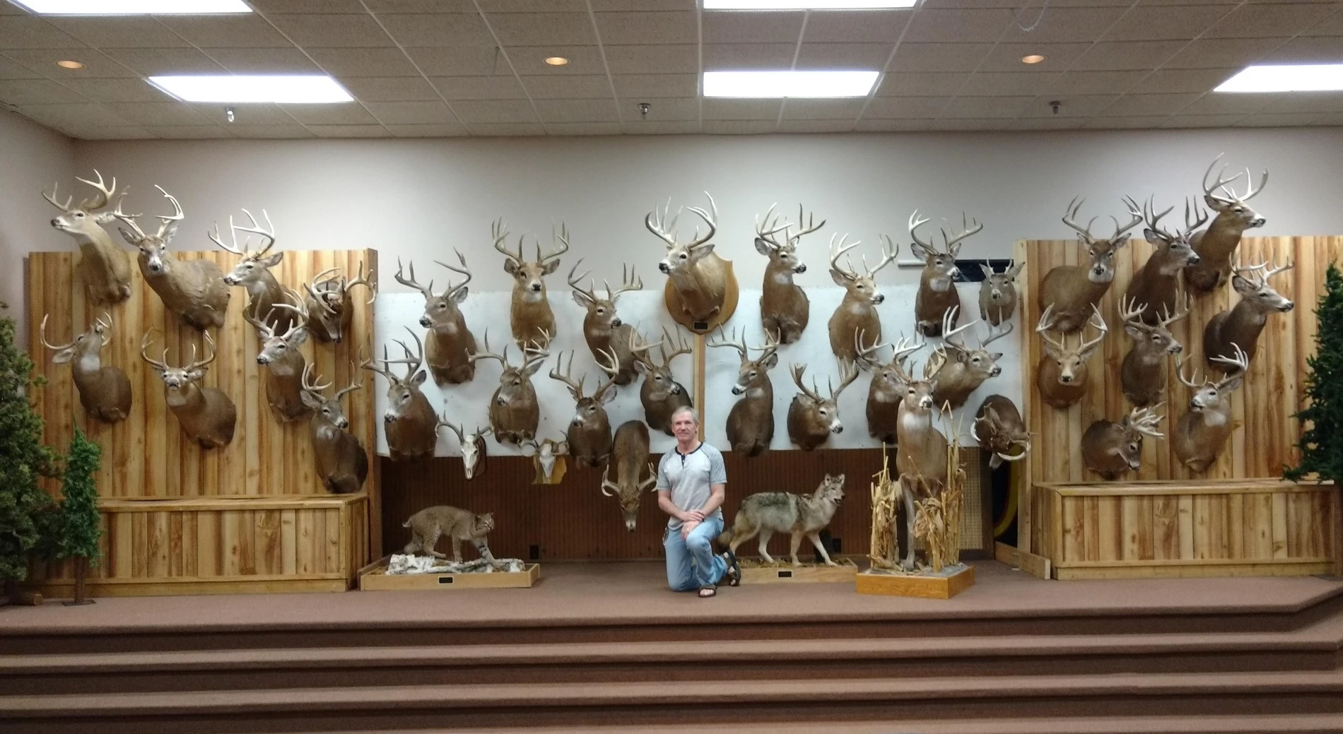 Well-known hunter John Eberhart kneels in front of a wall filled with the mounts of trophy deer he took. 