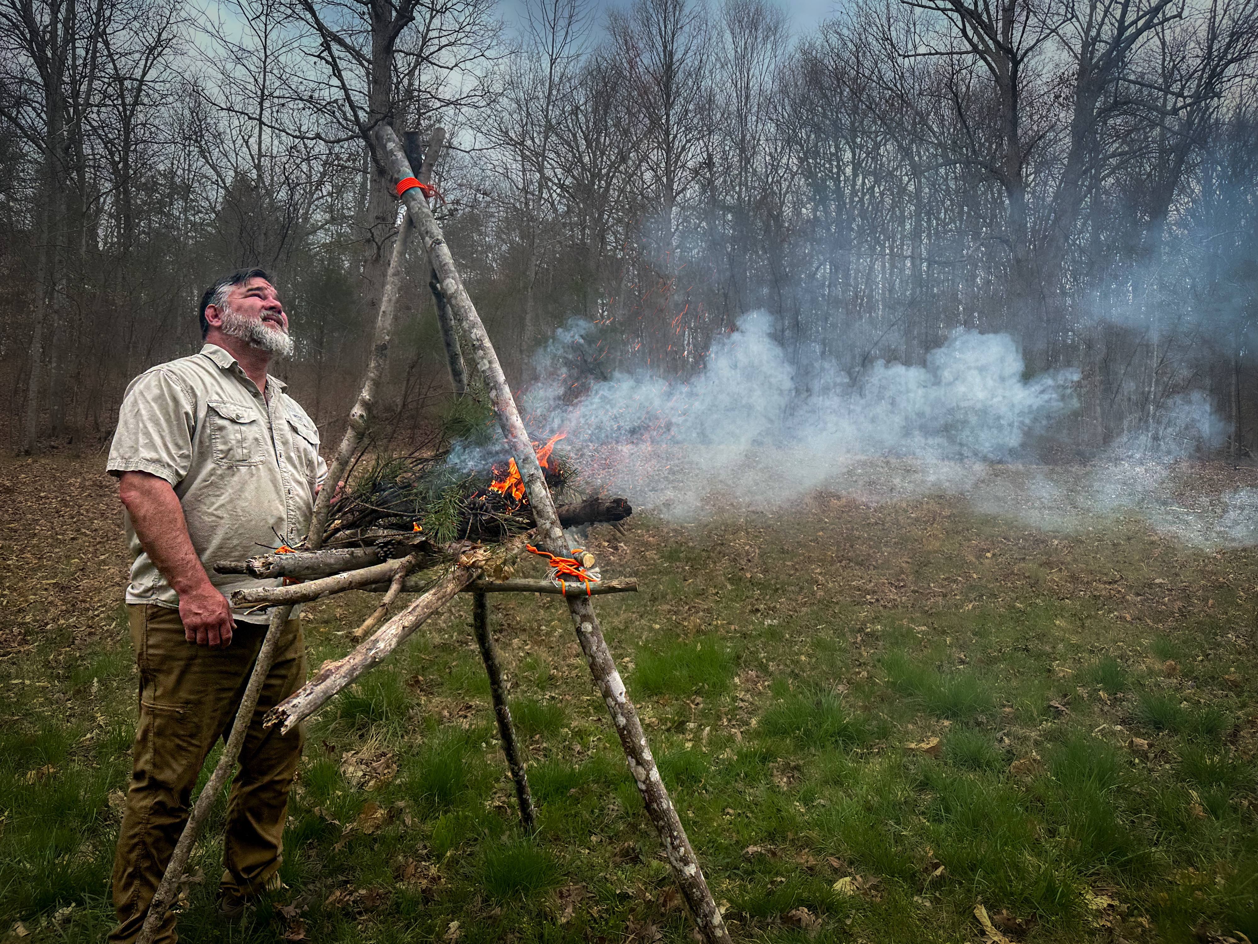 A man in a white shirt looks up as a signal fire burns smoke