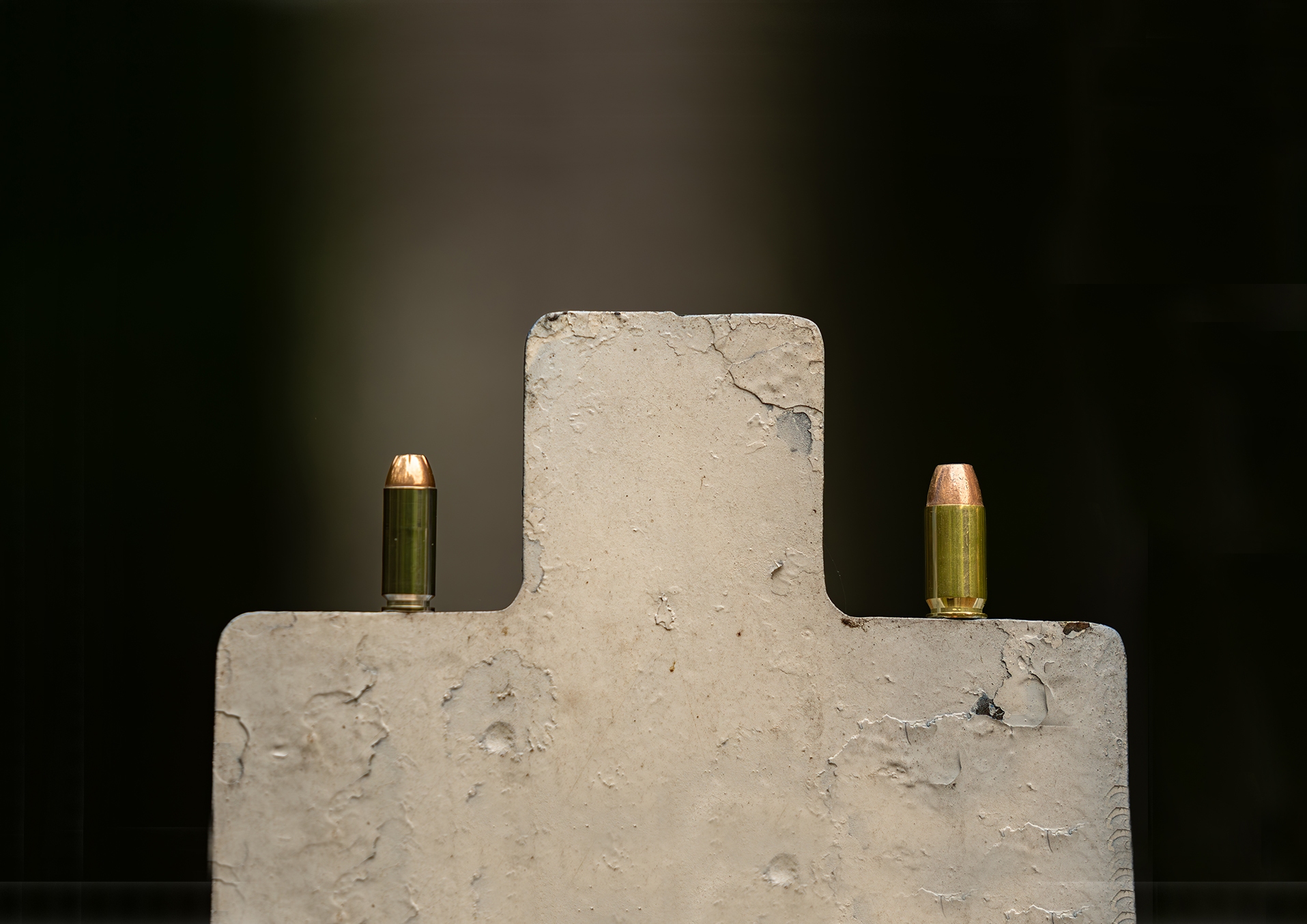 Two pistol cartridges standing on top of a steel target for 10mm vs 45 ACP. 