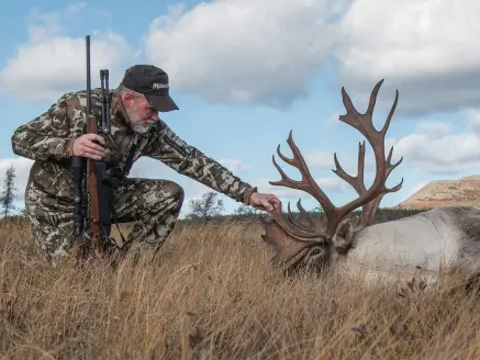 A hunter kneels next to a large caribou.