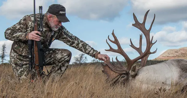 A hunter kneels next to a large caribou.