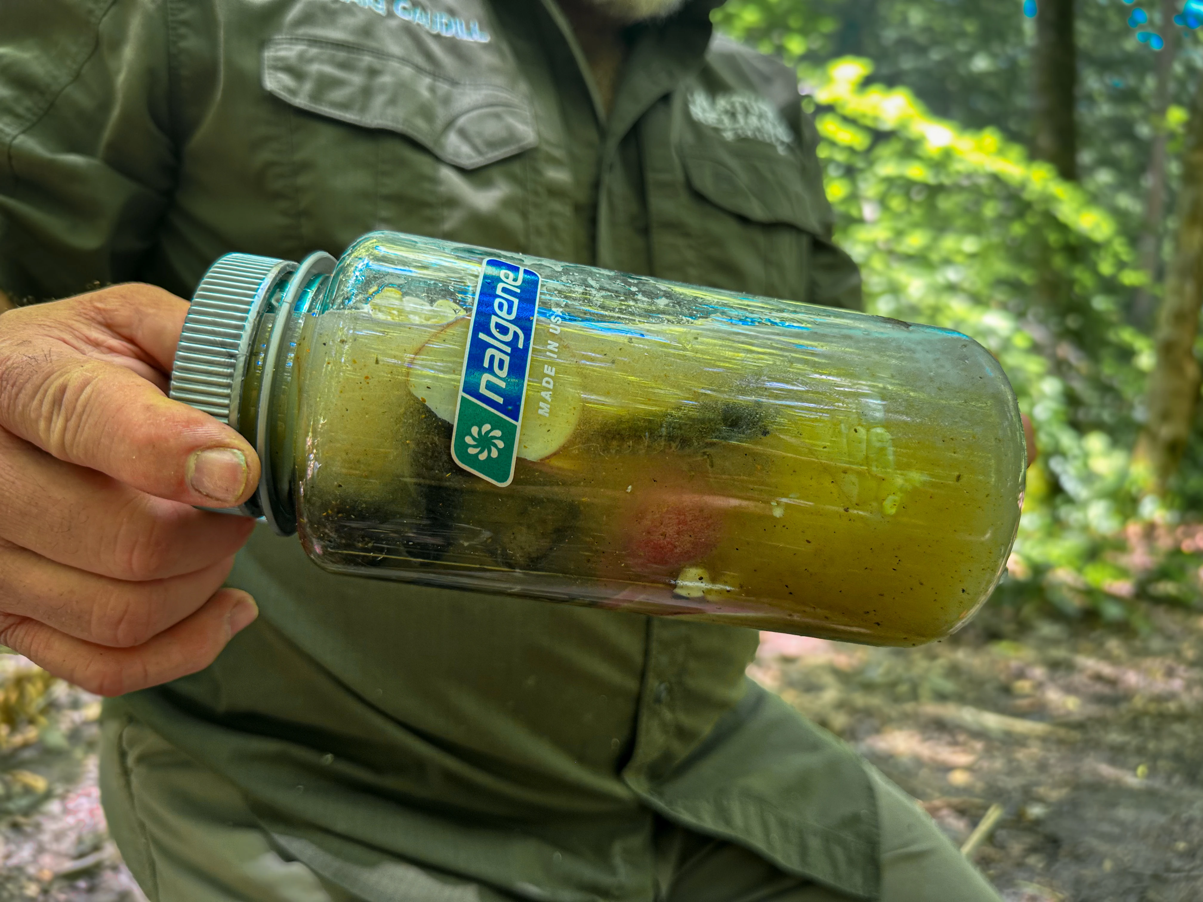 A person holds a Nalgene bottle full of hot rocks and crawfish