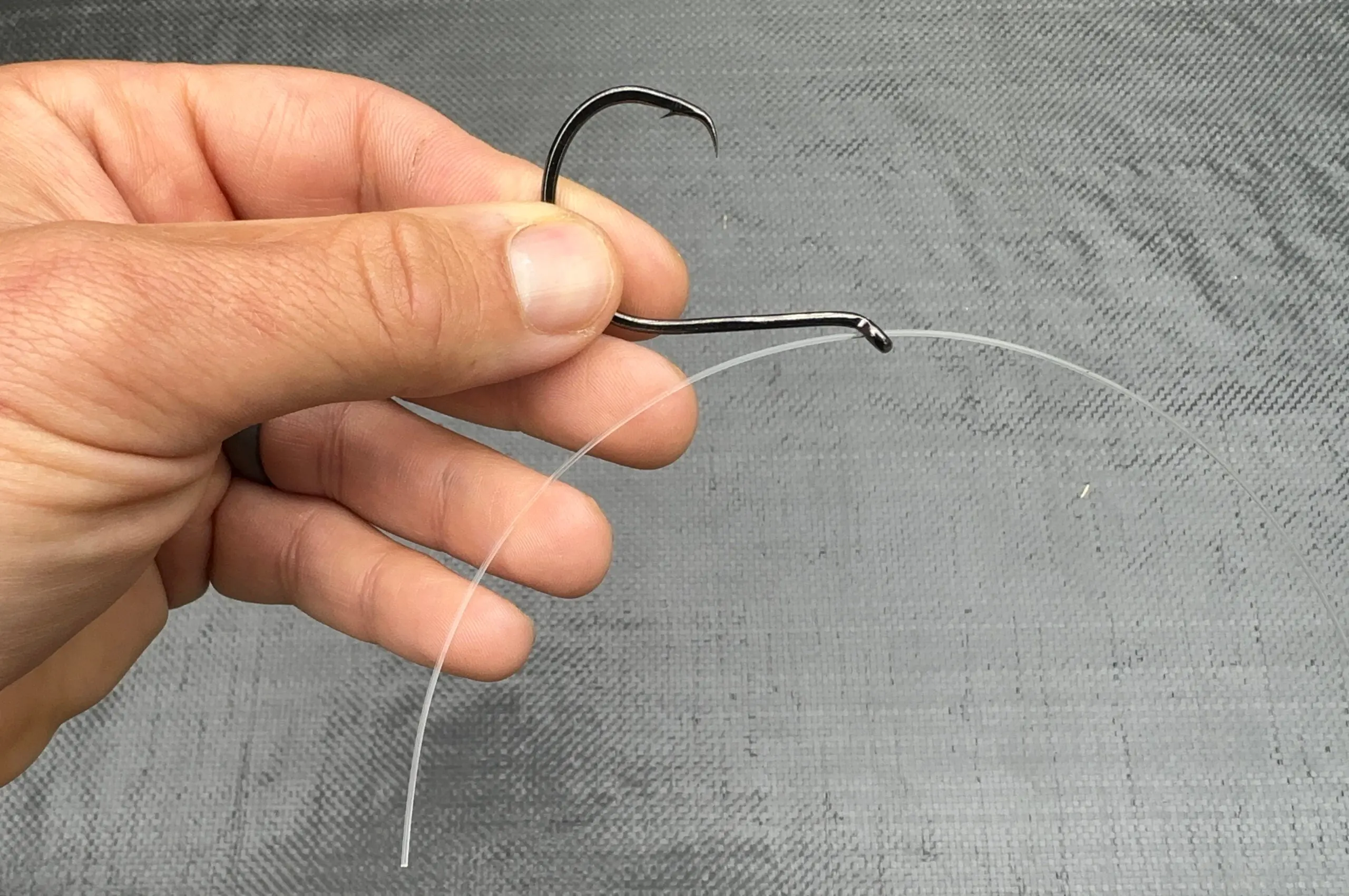 The first step in threading fishing line through a fishing hook to snell a hook