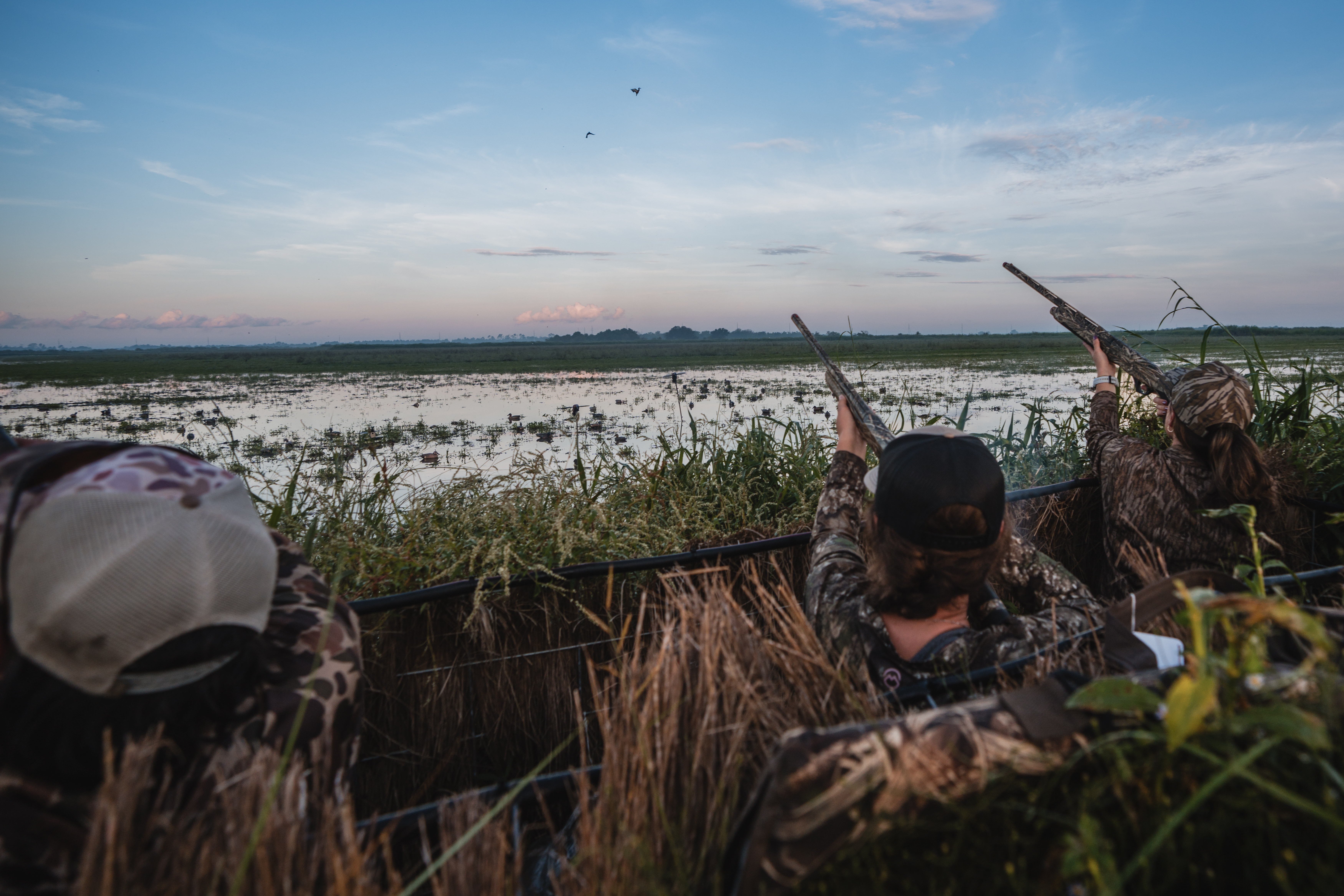 Duck hunters shoot shotguns from a pit blind