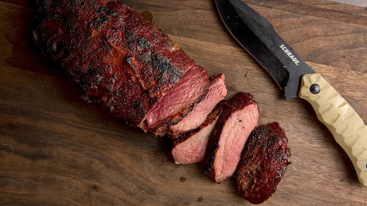 Smoked venison backstrap on a cutting board with a knife