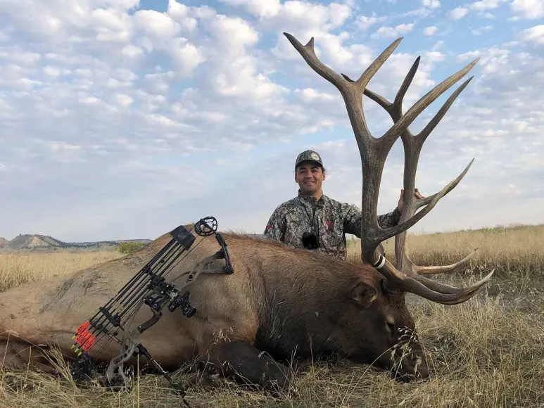 Yahsti Perkinskiller kneeling behind a giant bull elk