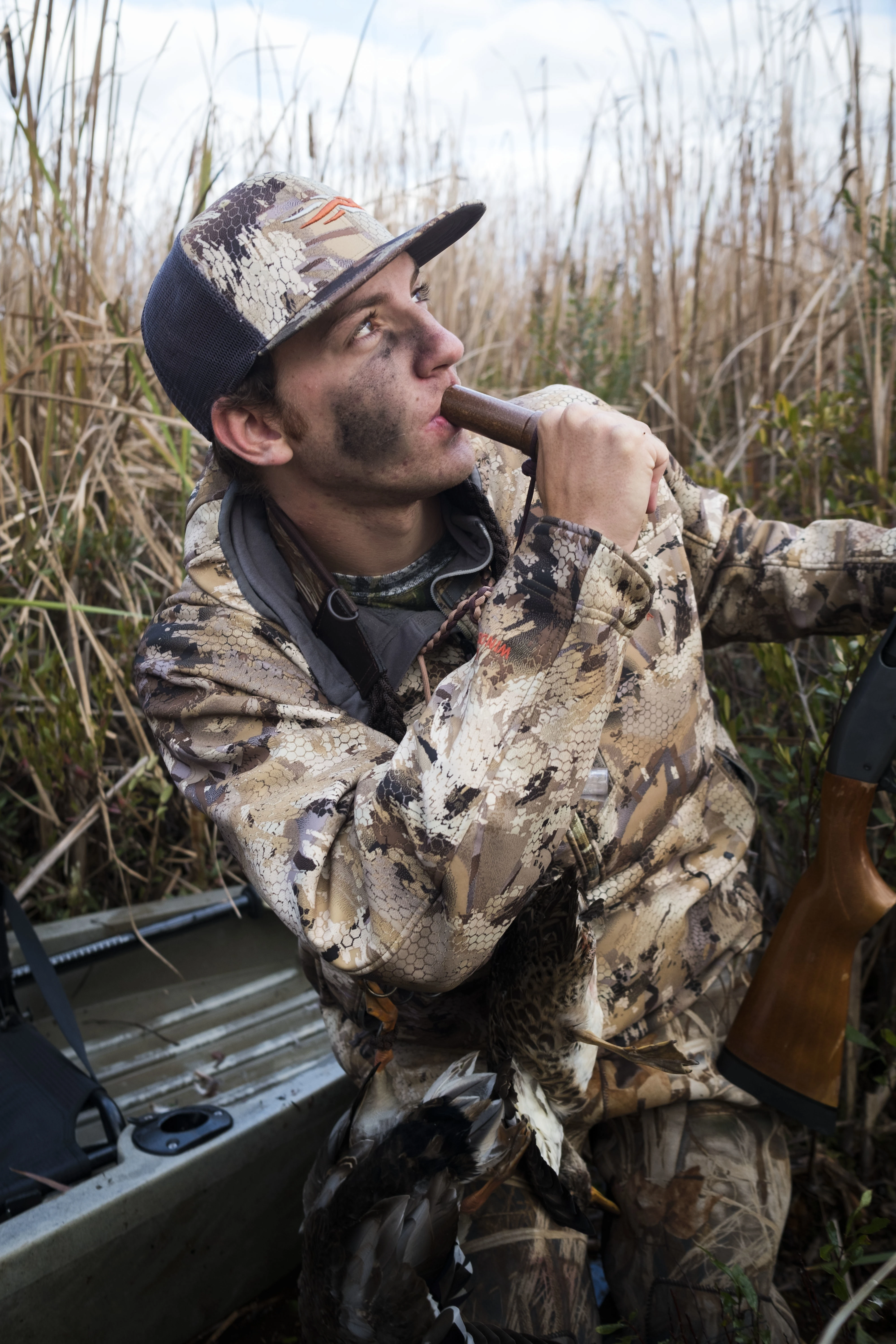 A duck hunter blows a duck call while looking toward the sky