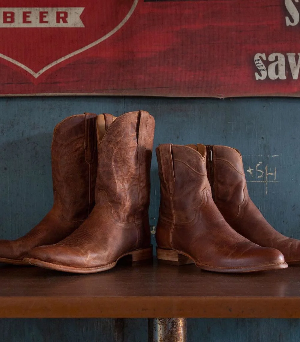 Two pairs of Tecovas cowboy boots sitting on bench