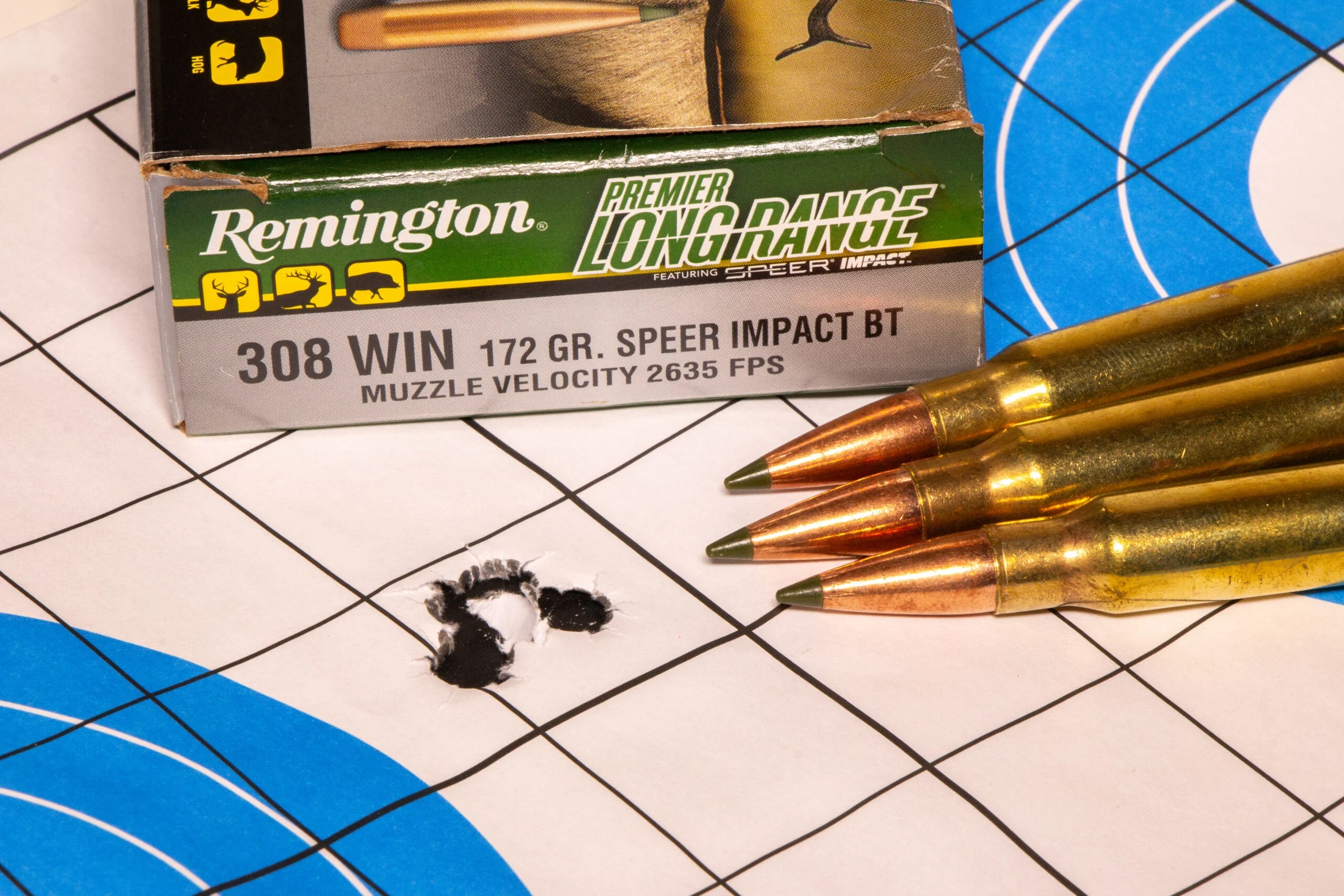 A rifle target showing a very small group with a box of Remington ammo and three loose cartridges