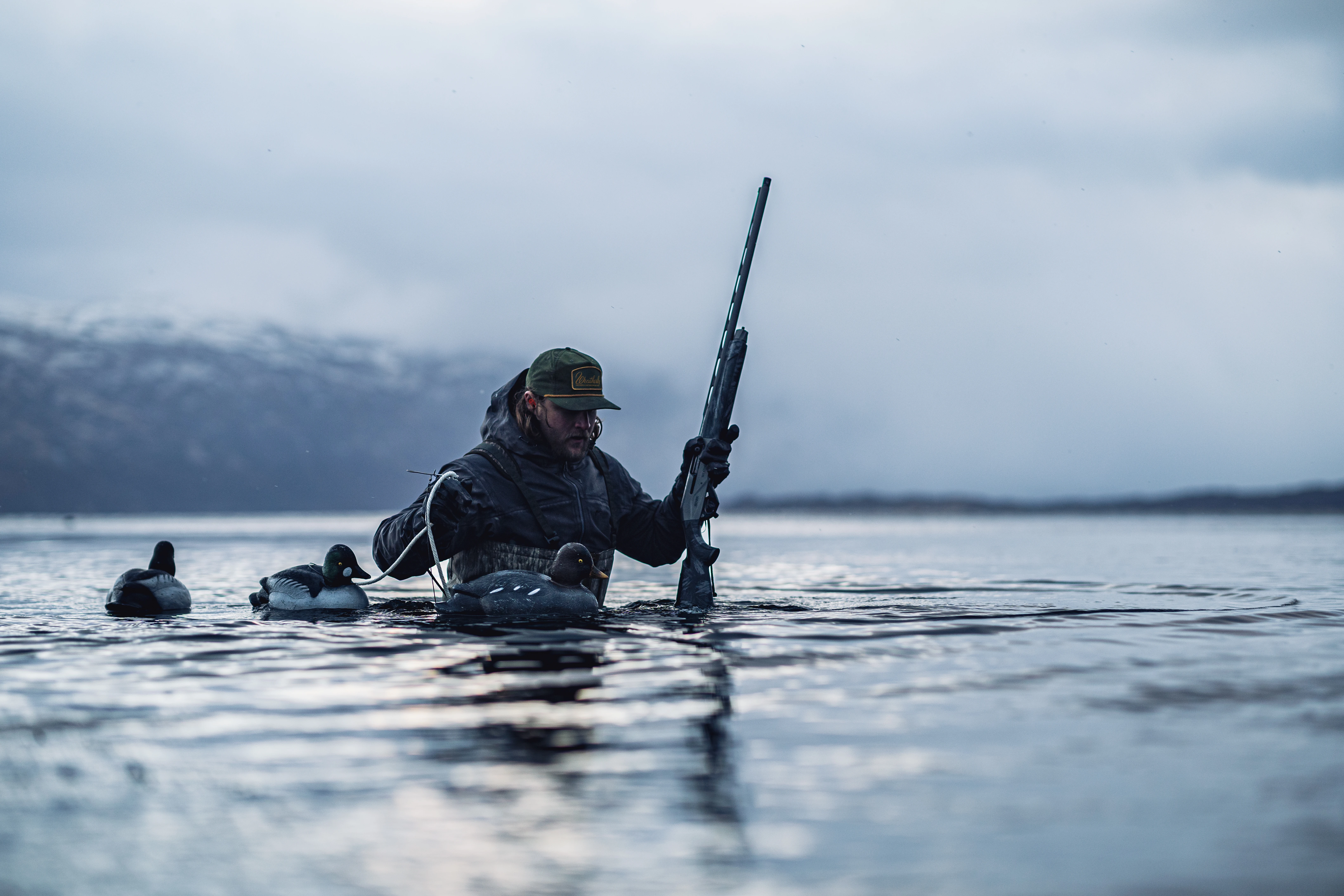 A waterfowl hunter wades waist-deep while setting decoys and holding a new Weatherby shotgun. 