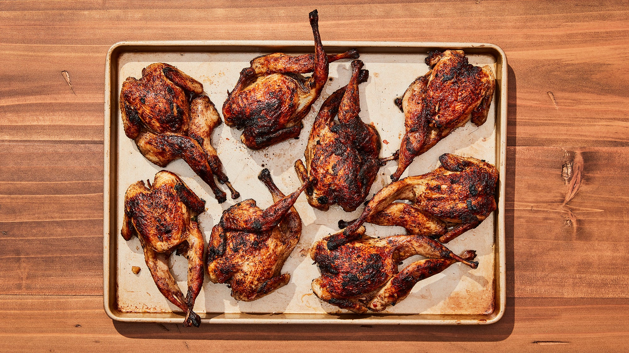 spatchcocked, cooked quail on metal tray and wood counter