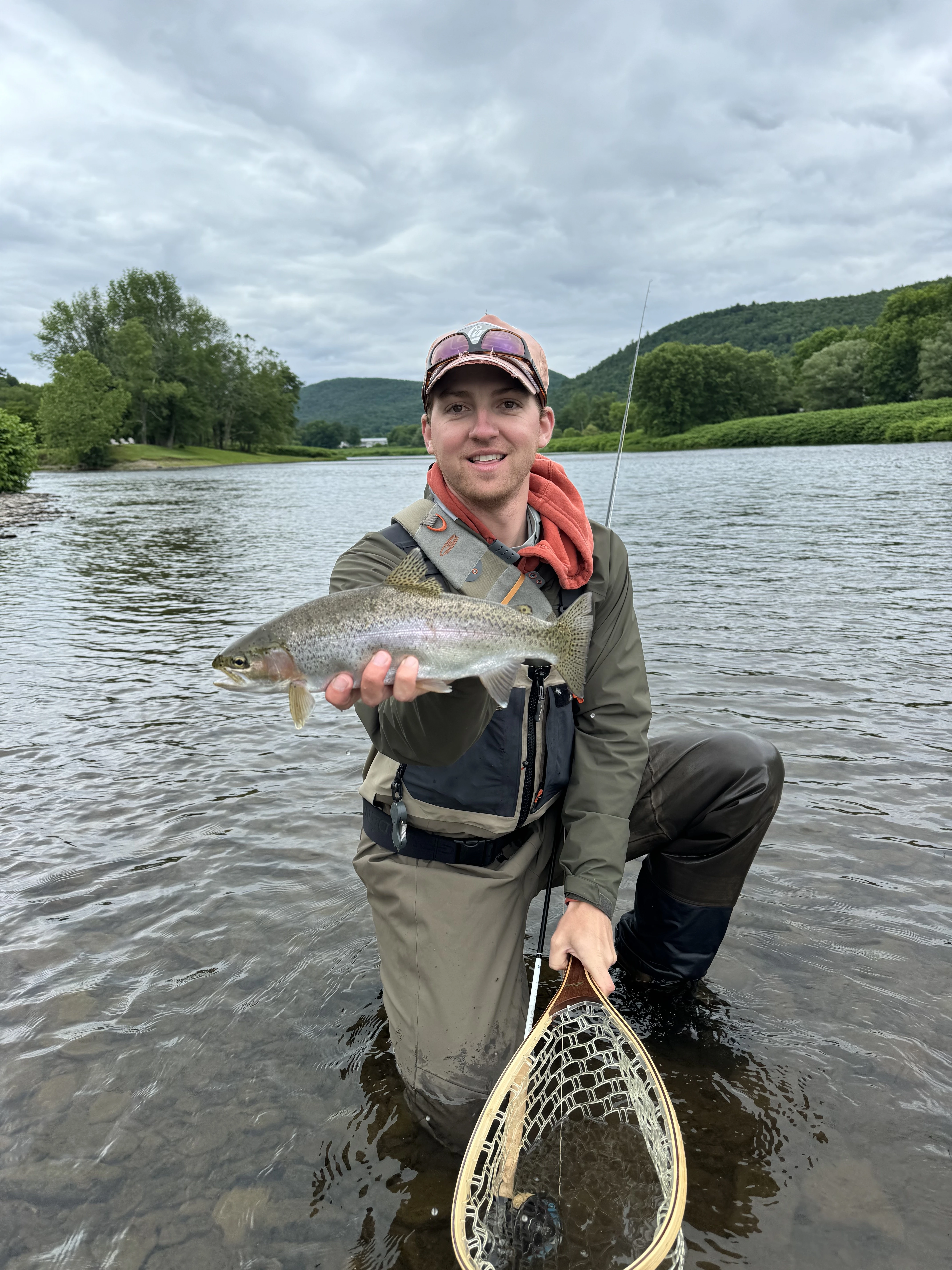 Fly fisherman holds up rainbow trout in a river